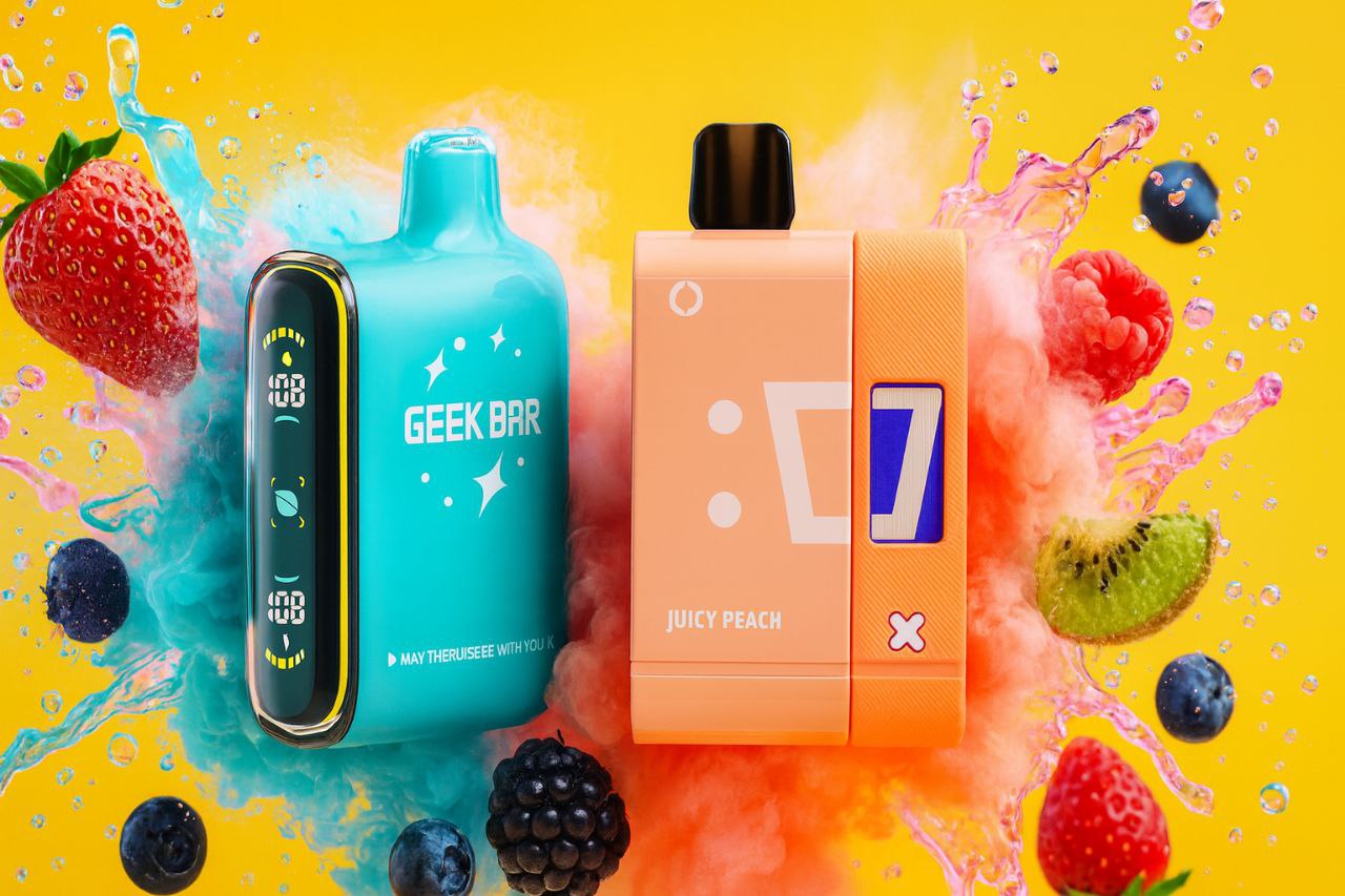 A bright, high-energy image showcases two vaporizers, one teal and one peach-orange, against a vivid yellow background. The devices are surrounded by dramatic splashes of blue and pink liquid and mist. Fresh fruits, including a large strawberry, raspberries, blueberries, and a slice of kiwi, are scattered around the products, suggesting a sweet and refreshing flavor profile.