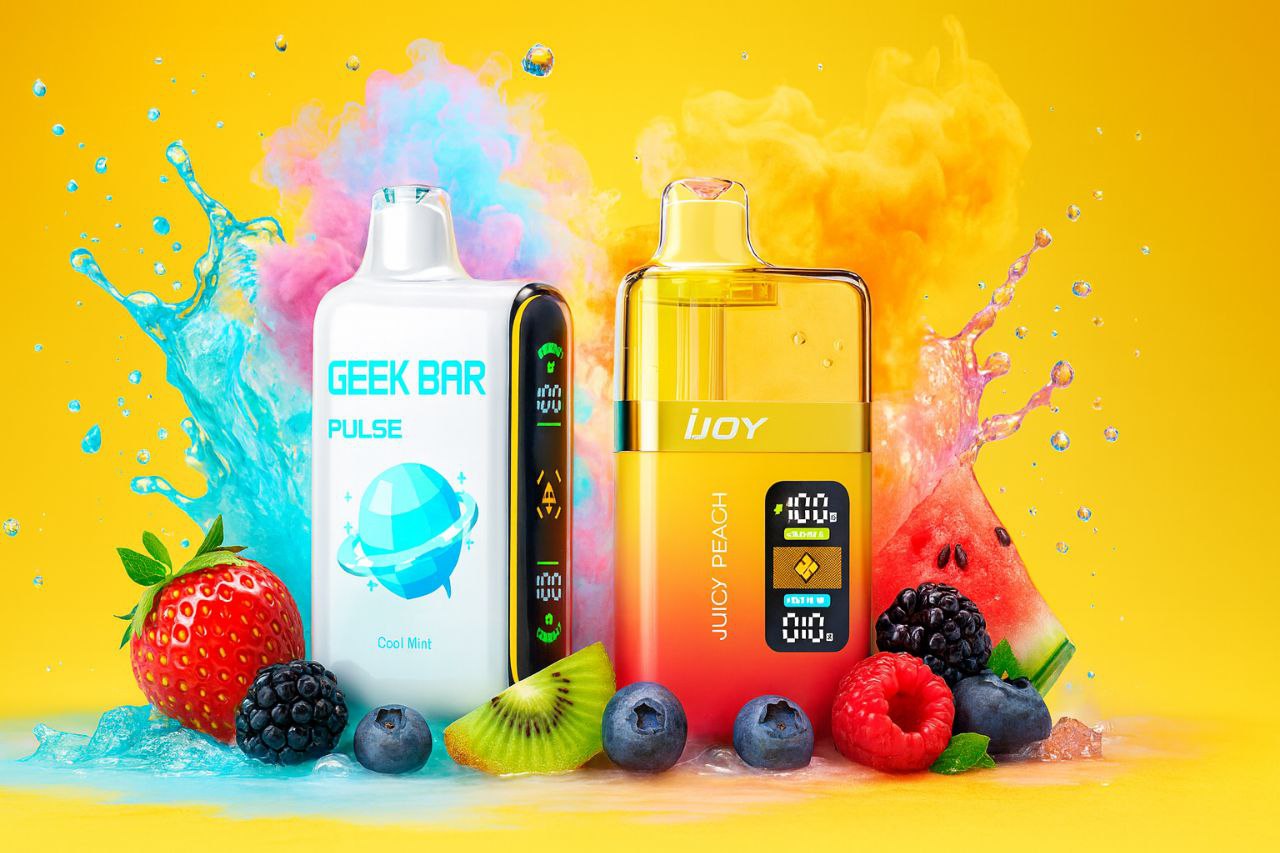 A bright, high-contrast image showcasing two sleek vaporizers, one white and one yellow/orange, against a sunny background. The products are dramatically framed by splashes of blue and pink water/smoke, and surrounded by fresh, vibrant fruits like strawberries, blueberries, kiwi, and a slice of watermelon. The overall composition is energetic and suggests a theme of cooling and fruity flavors.